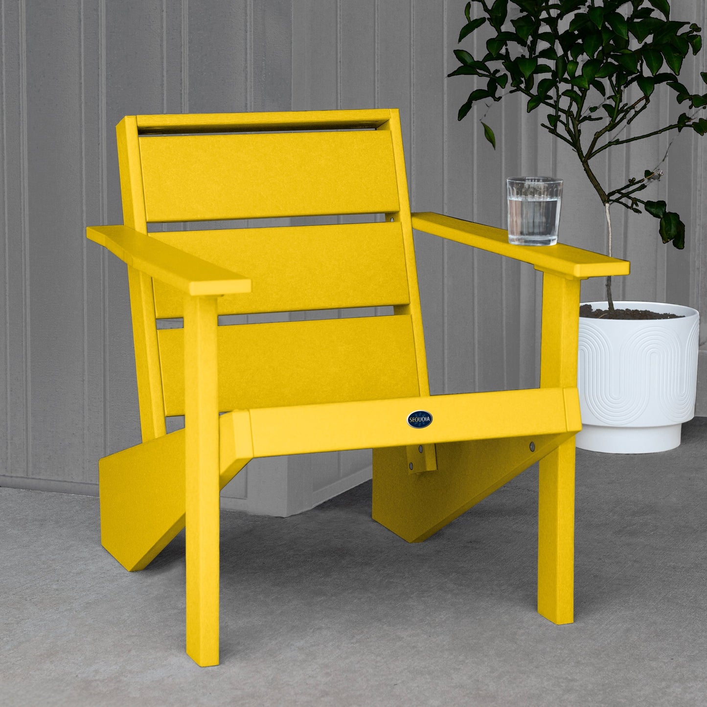 Sequoia Professional Outdoor Sunrise Coast Modern Adirondack Chair sitting in front of a gray background with a potted plant and a glass of water on the arm. Durable Outdoor Patio Furniture 15 year Residential or 7 year Commercial Warranty