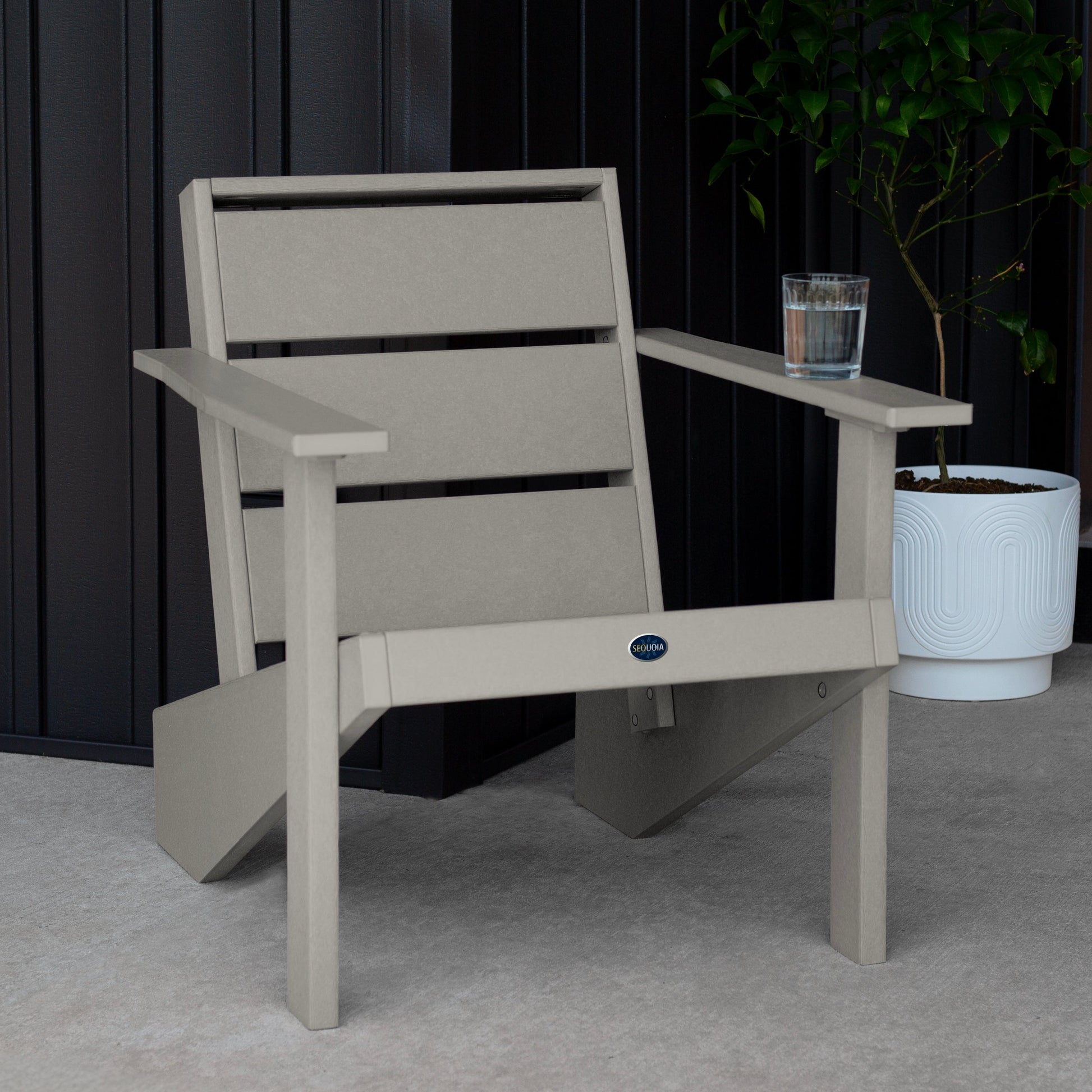Sequoia Professional Outdoor Sunrise Coast Modern Adirondack Chair sitting in front of a gray background with a potted plant and a glass of water on the arm. Durable Outdoor Patio Furniture 15 year Residential or 7 year Commercial Warranty