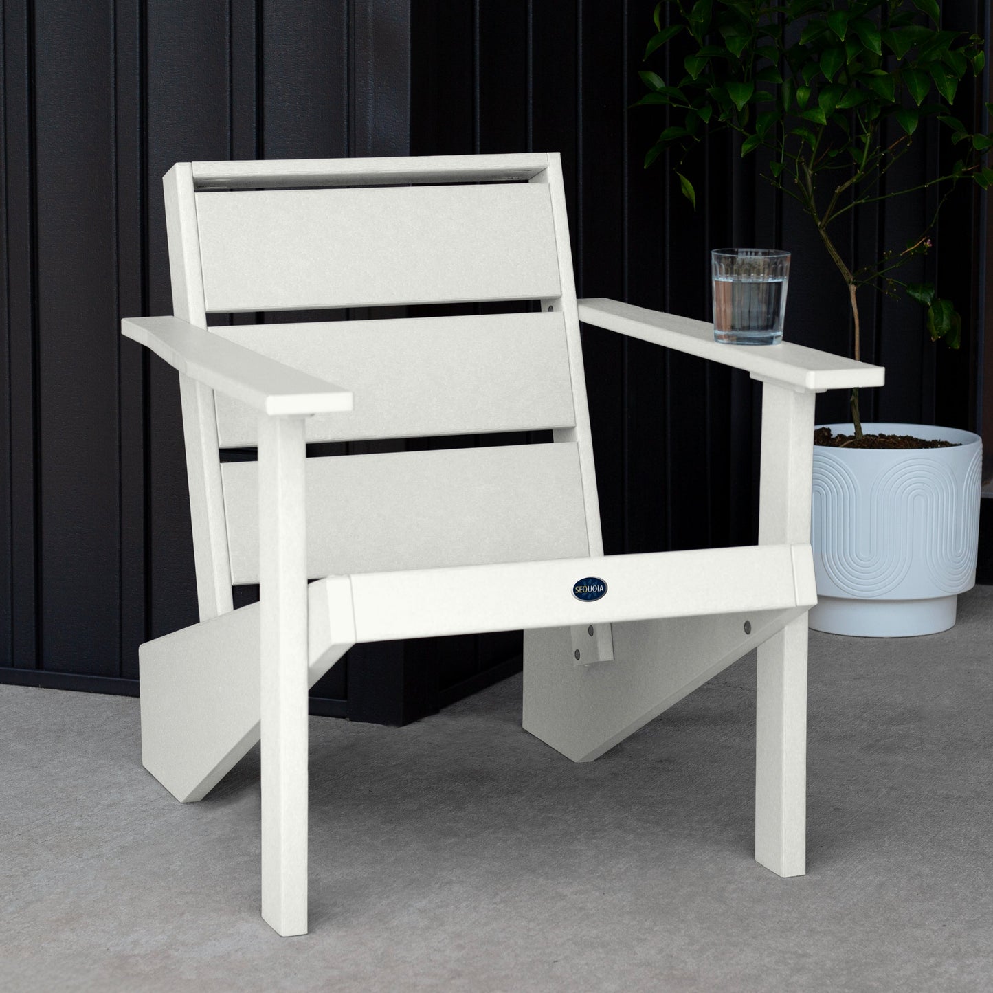 Sequoia Professional Outdoor Sunrise Coast Modern Adirondack Chair sitting in front of a gray background with a potted plant and a glass of water on the arm. Durable Outdoor Patio Furniture 15 year Residential or 7 year Commercial Warranty
