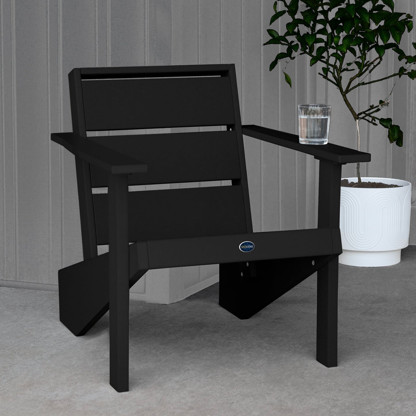 Sequoia Professional Outdoor Sunrise Coast Modern Adirondack Chair sitting in front of a gray background with a potted plant and a glass of water on the arm. Durable Outdoor Patio Furniture 15 year Residential or 7 year Commercial Warranty