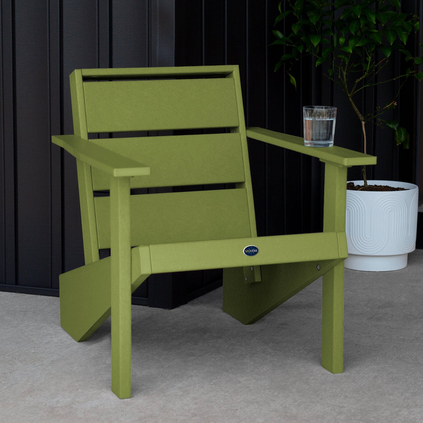 Sequoia Professional Outdoor Sunrise Coast Modern Adirondack Chair sitting in front of a gray background with a potted plant and a glass of water on the arm. Durable Outdoor Patio Furniture 15 year Residential or 7 year Commercial Warranty