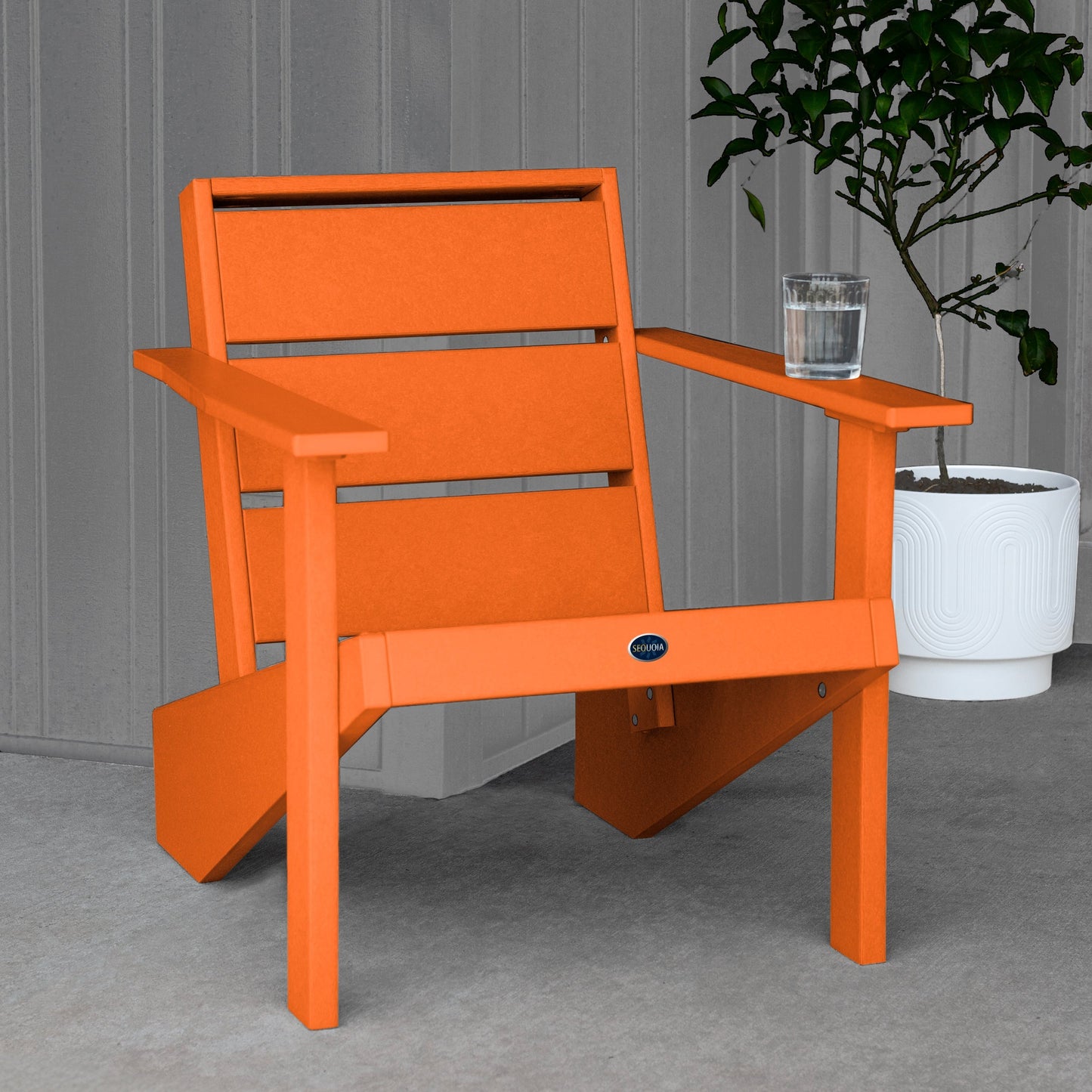 Sequoia Professional Outdoor Sunrise Coast Modern Adirondack Chair sitting in front of a gray background with a potted plant and a glass of water on the arm. Durable Outdoor Patio Furniture 15 year Residential or 7 year Commercial Warranty
