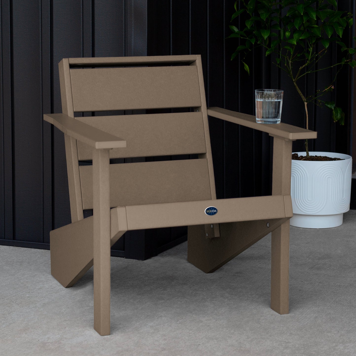 Sequoia Professional Outdoor Sunrise Coast Modern Adirondack Chair sitting in front of a gray background with a potted plant and a glass of water on the arm. Durable Outdoor Patio Furniture 15 year Residential or 7 year Commercial Warranty