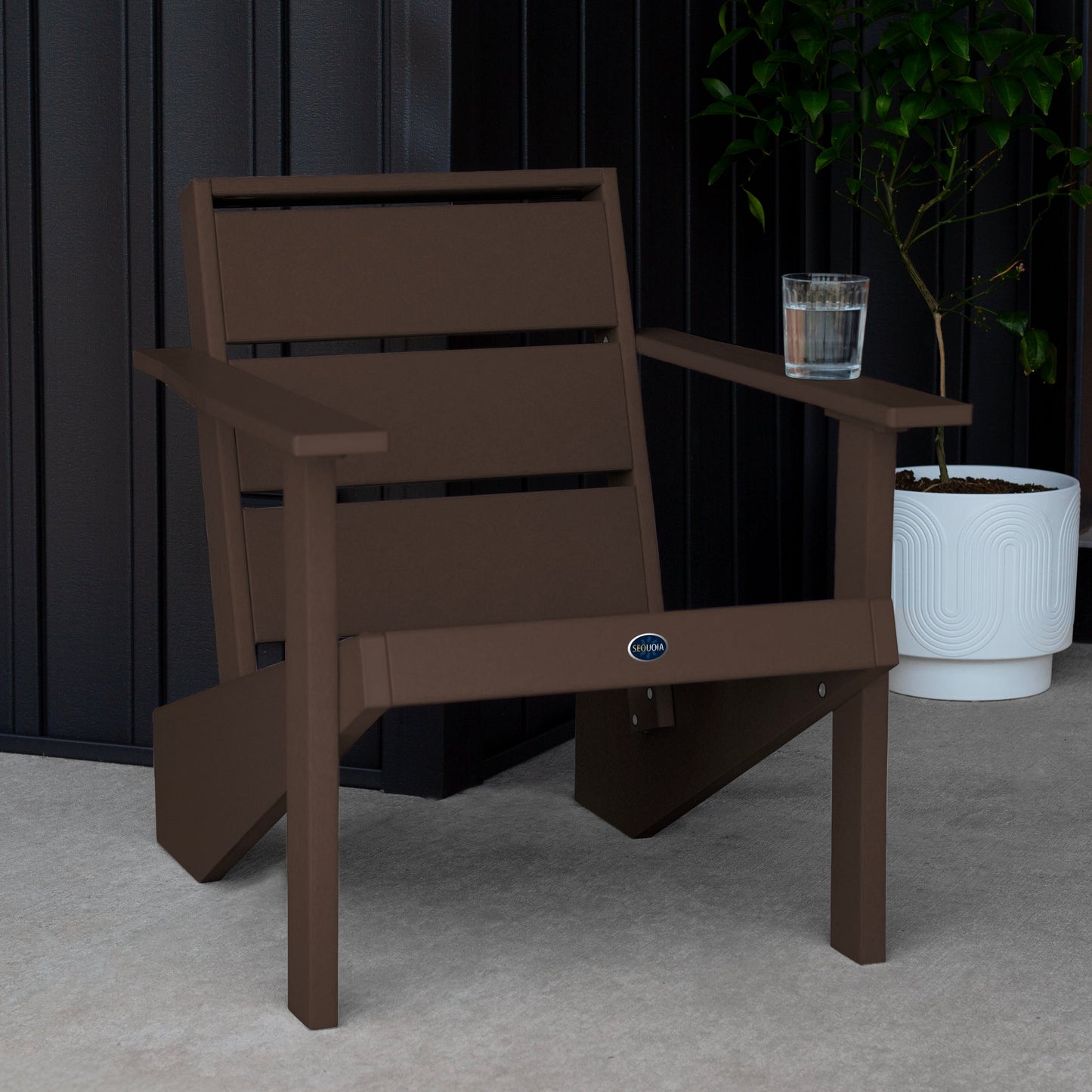 Sequoia Professional Outdoor Sunrise Coast Modern Adirondack Chair sitting in front of a gray background with a potted plant and a glass of water on the arm. Durable Outdoor Patio Furniture 15 year Residential or 7 year Commercial Warranty