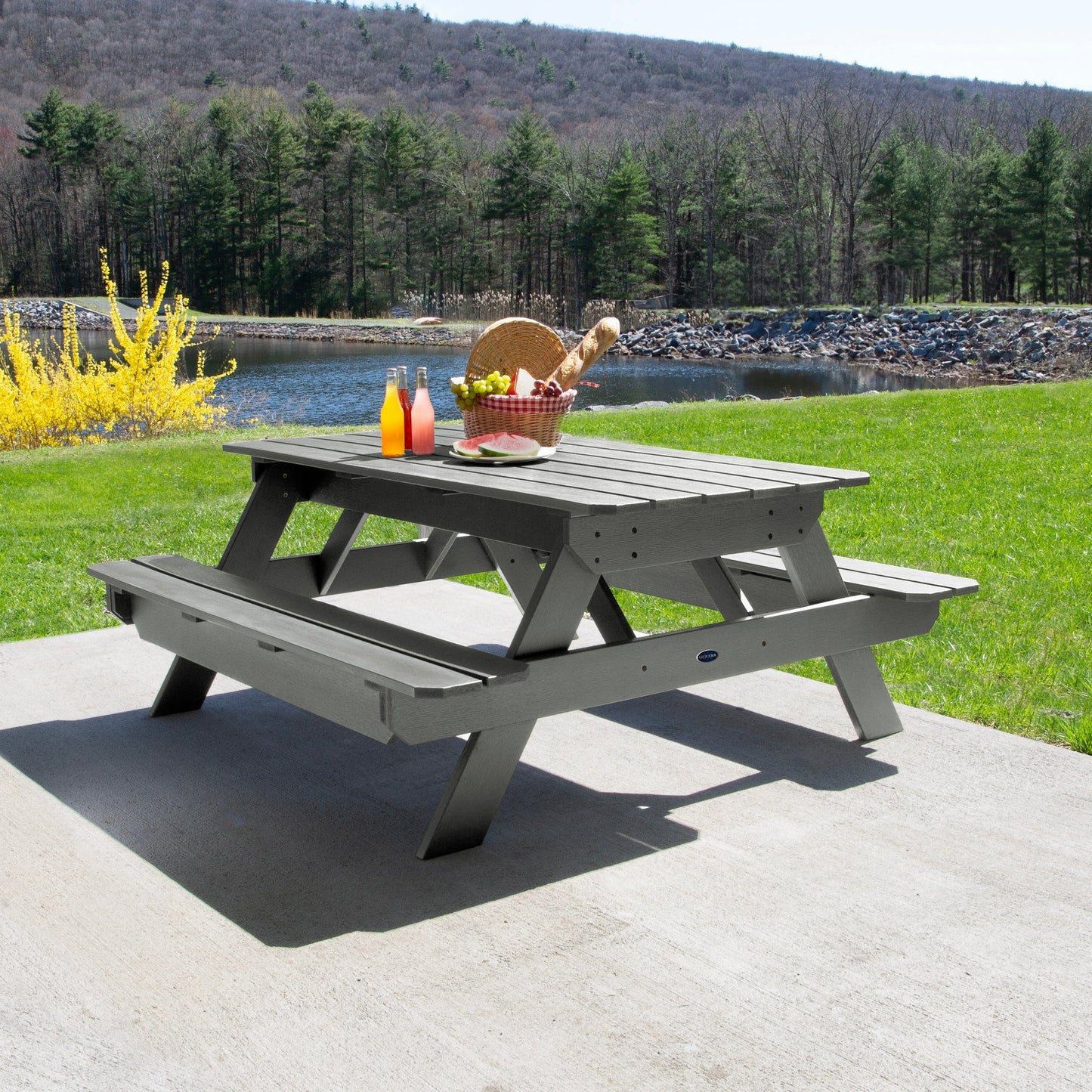Ember & Oasis presents the Homestead 6' Picnic Table in a beautiful outdoor setting next to a pond with trees and a mountain background. This is manufactured 100% in the USA from high-quality poly lumber and comes with a limited 15 year residential and 7 year commercial warranty! 