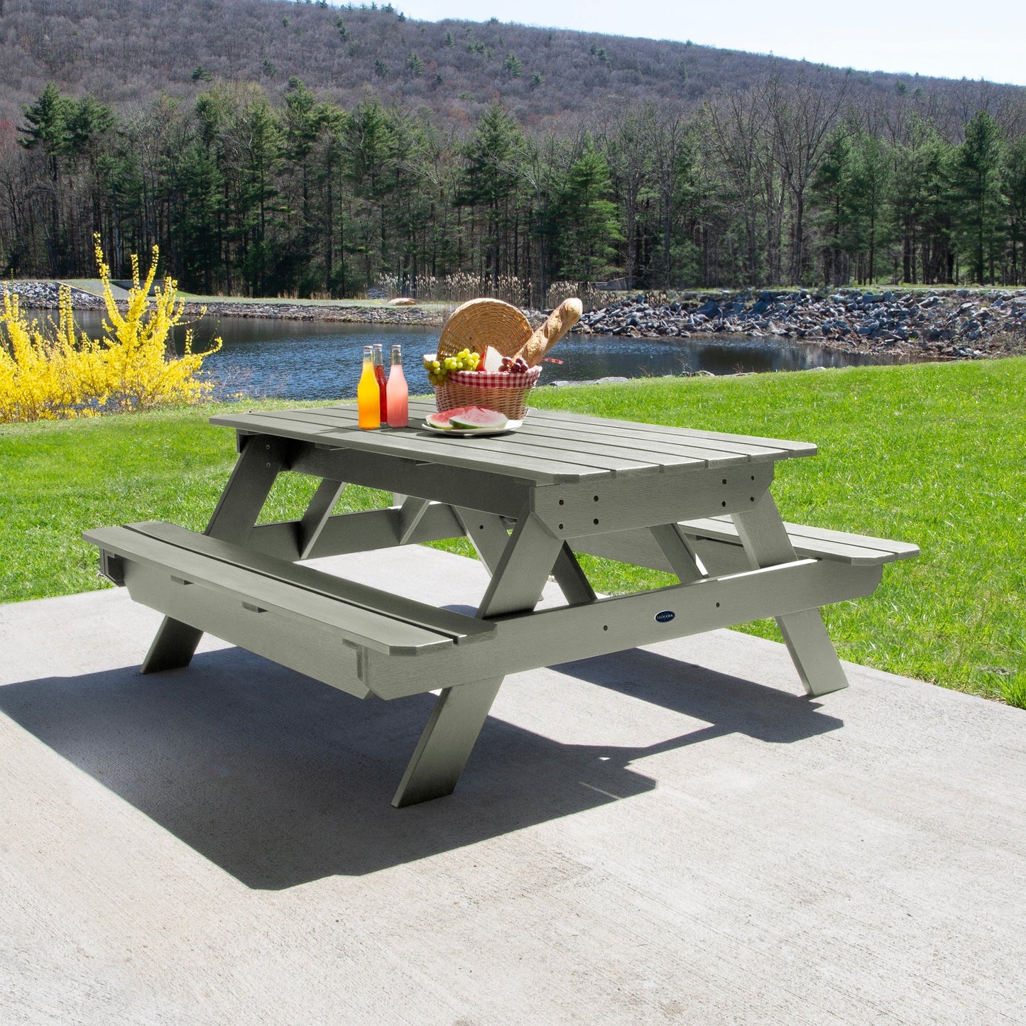 Ember & Oasis presents the Homestead 6' Picnic Table in a beautiful outdoor setting next to a pond with trees and a mountain background. This is manufactured 100% in the USA from high-quality poly lumber and comes with a limited 15 year residential and 7 year commercial warranty! 