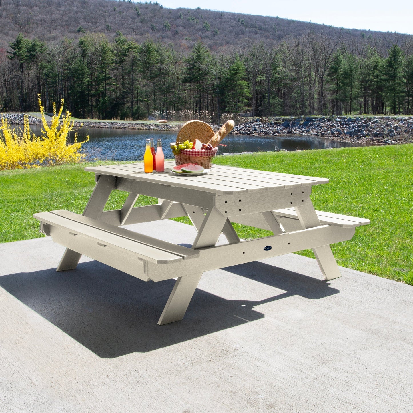 Ember & Oasis presents the Homestead 6' Picnic Table in a beautiful outdoor setting next to a pond with trees and a mountain background. This is manufactured 100% in the USA from high-quality poly lumber and comes with a limited 15 year residential and 7 year commercial warranty! 