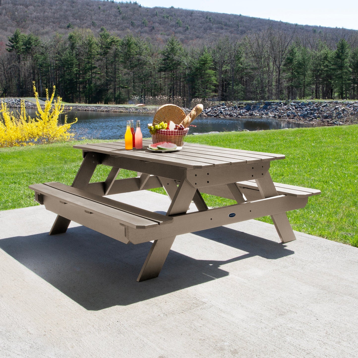 Ember & Oasis presents the Homestead 6' Picnic Table in a beautiful outdoor setting next to a pond with trees and a mountain background. This is manufactured 100% in the USA from high-quality poly lumber and comes with a limited 15 year residential and 7 year commercial warranty! 